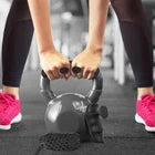 Person lifting a black kettlebell with gym grips.